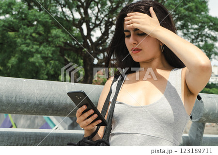 Young latin woman feeling stressed while reading bad news on smartphone Young latin woman feeling stressed while reading bad news on smartphone 123189711