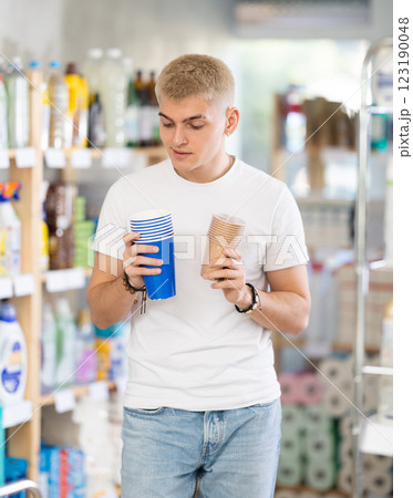 Guy selects and purchases paper cups in the household goods section of supermarket 123190048