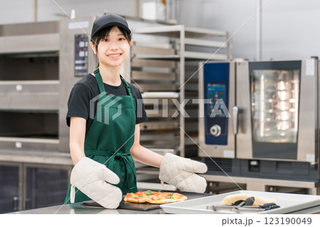 オーブンからピザを取り出す女性調理スタッフ 123190049