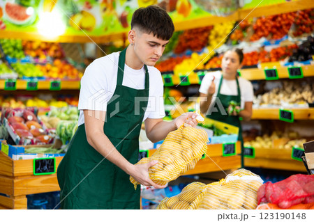 Male shop assistant lays potatoes on counter in grocery shop Male shop assistant lays potatoes on counter in grocery shop 123190148