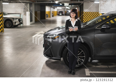 Caucasian businesswoman in parking garage holding cash, dressed in formal attire, exuding confidence and success. Represents corporate lifestyle, finance, middle-aged professional woman. 123191312