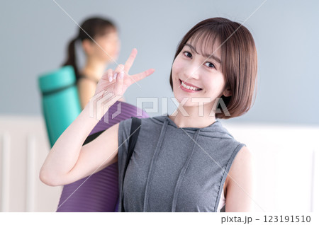 ヨガマットを持ちながらVサインする笑顔の若い女性 ヨガマットを持ちながらVサインする笑顔の若い女性 123191510