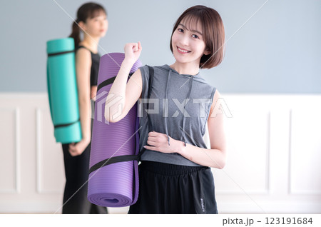 ヨガマットを持ちながらガッツポーズする笑顔の若い女性 ヨガマットを持ちながらガッツポーズする笑顔の若い女性 123191684