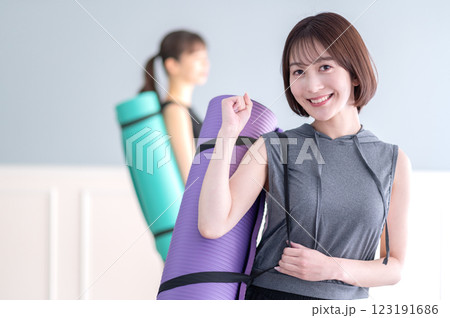 ヨガマットを持ちながらガッツポーズする笑顔の若い女性 ヨガマットを持ちながらガッツポーズする笑顔の若い女性 123191686