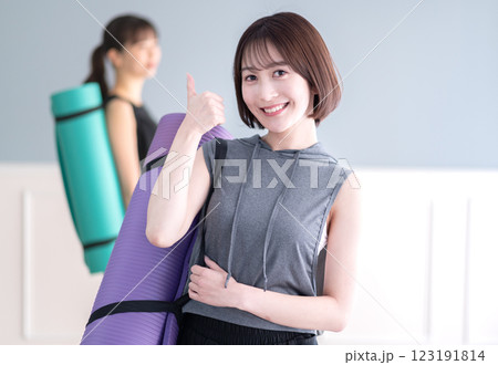 ヨガマットを持ちながらグッドポーズする笑顔の若い女性 123191814