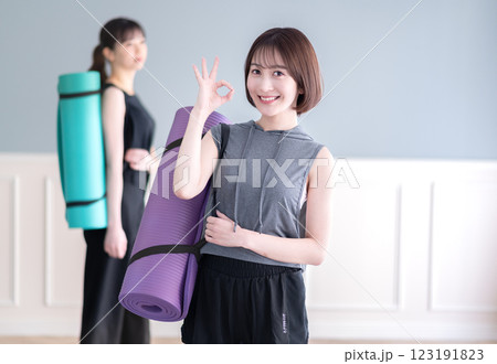 ヨガマットを持ちながらOKポーズする笑顔の若い女性 ヨガマットを持ちながらOKポーズする笑顔の若い女性 123191823