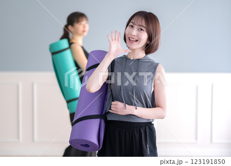 ヨガマットを持ちながら呼びかけるポーズする笑顔の若い女性 123191850