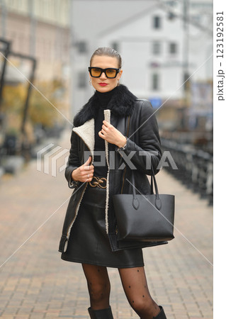 Stylish woman walking in a city street wearing a black leather jacket and sunglasses during autumn 123192581