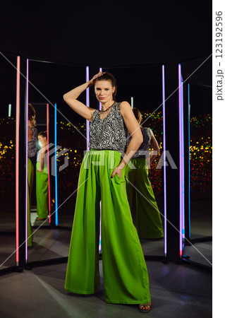 Model showcases vibrant green pants and patterned top in a stylish indoor setting with mirrors Model showcases vibrant green pants and patterned top in a stylish indoor setting with mirrors 123192596