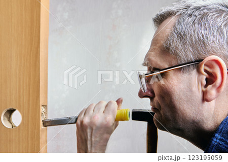 Chiseling groove in door leaf for latch installation, mortising cutting recess into wood to accommodate latch, using chisel to remove material. Chiseling groove in door leaf for latch installation, mortising cutting recess into wood to accommodate latch, using chisel to remove material. 123195059