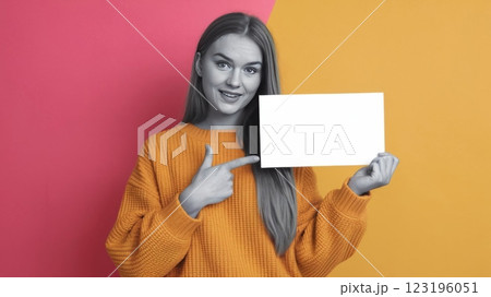 Cheerful Young Woman in Knitted Sweater Pointing at Blank Card Against Solid Background - Mockup Template for Advertisement or Announcement 123196051