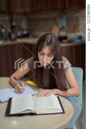 Focused female student learning Bible and preparing exam at home, reading textbook and taking notes Focused female student learning Bible and preparing exam at home, reading textbook and taking notes 123196084