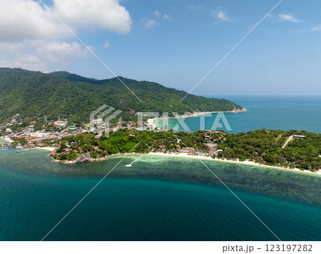 A lush green hillside descending to a rocky coastline with vibrant blue waters stretching to the horizon. Rin Nai Beach. Haad Rin. Ko Pha Ngan, Thailand. 123197282