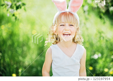 Easter egg hunt. Girl child Wearing Bunny Ears Running To Pick Up Egg In Garden. Easter tradition. Baby with basket full of colorful eggs. Easter egg hunt. Girl child Wearing Bunny Ears Running To Pick Up Egg In Garden. Easter tradition. Baby with basket full of colorful eggs. 123197954