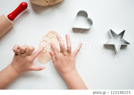 Child hands crafting with dough and cookie cutters in kitchen setting Child hands crafting with dough and cookie cutters in kitchen setting 123198155
