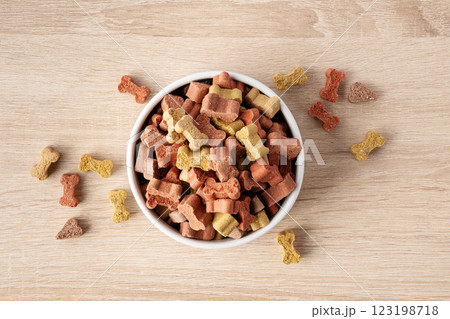 Dry dog food in a shape of bones in bowl on wooden floor background top view. Plate full of mineral healthy dog food. Pet snack in white bowl on floor. 123198718