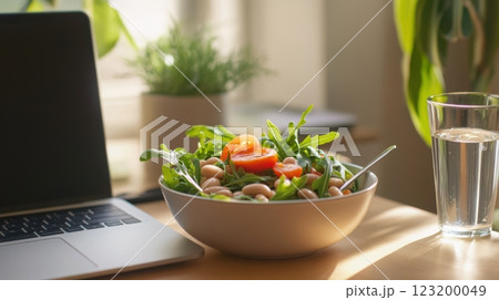 A healthy office lunch with bean salad, white beans, arugula, and cherry tomatoes, served on a desk beside a laptop and water glass. A healthy office lunch with bean salad, white beans, arugula, and cherry tomatoes, served on a desk beside a laptop and water glass. 123200049