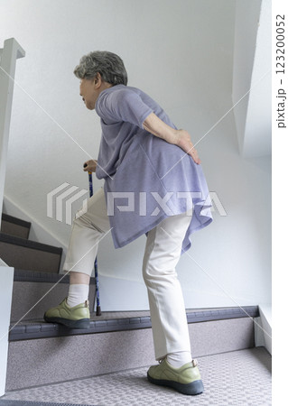 腰をおさえながら階段をあがるシニア女性 123200052