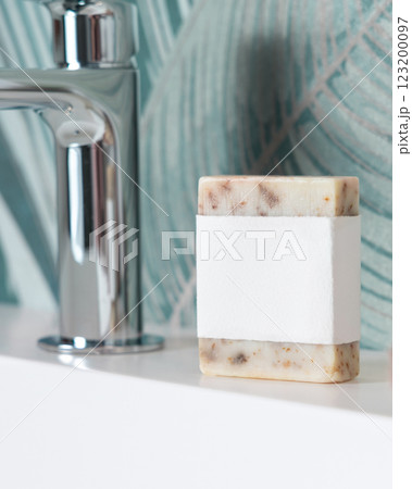 Beige soap with blank label on basin near faucet in tropical bathroom close up, mockup 123200097