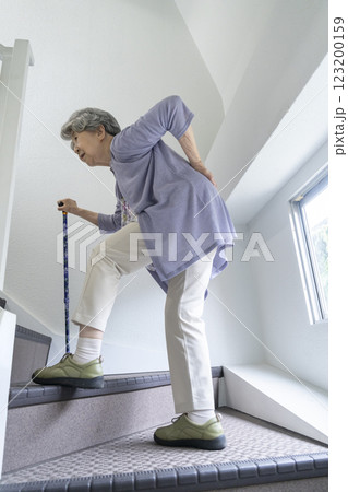 腰をおさえながら階段をあがるシニア女性 腰をおさえながら階段をあがるシニア女性 123200159