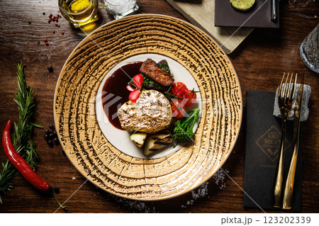 Gold-plated beef steak with grilled vegetables, cherry tomatoes, and a rich sauce. Gourmet dish garnished with edible flowers, served on an elegant plate in a fine dining restaurant Gold-plated beef steak with grilled vegetables, cherry tomatoes, and a rich sauce. Gourmet dish garnished with edible flowers, served on an elegant plate in a fine dining restaurant 123202339