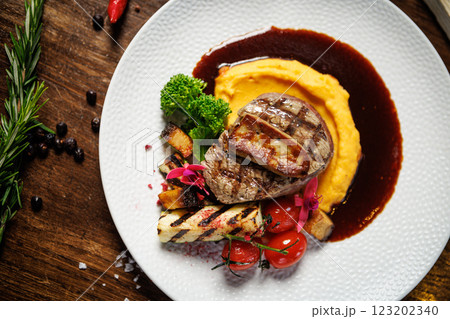 Tender beef medallion with foie gras, paired with smooth mashed sweet potatoes, grilled vegetables, and cherry tomatoes. Fine dining experience with artistic plating 123202340
