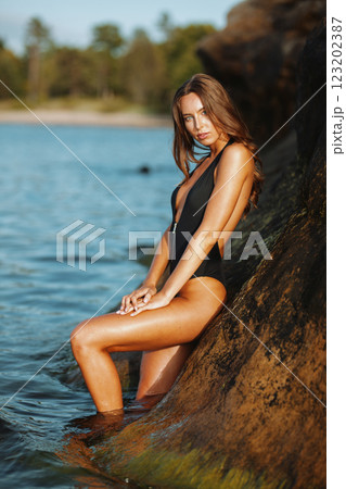 Sunlit beach portrait of a woman in a black swimsuit 123202387