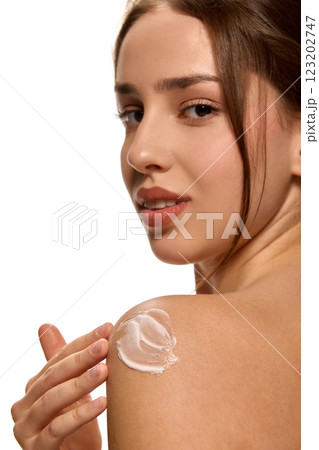 Young woman applying moisturizing cream, beauty product on shoulder and looking at camera against white background. Young woman applying moisturizing cream, beauty product on shoulder and looking at camera against white background. 123202747