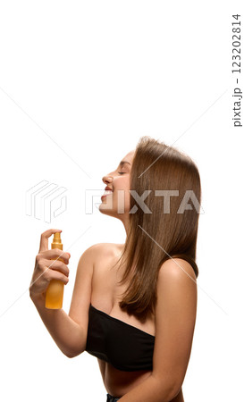 Young happy woman in black top tilting head back while spraying hair, enjoying beauty routine against white studio background. Young happy woman in black top tilting head back while spraying hair, enjoying beauty routine against white studio background. 123202814