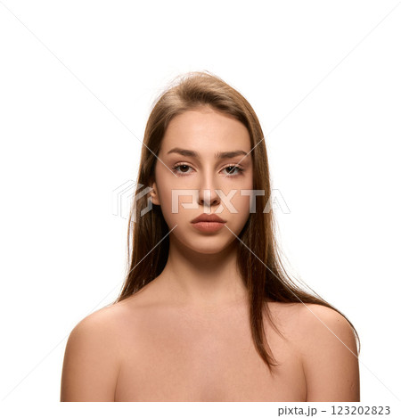 Portrait of young woman with natural makeup looking straight with calm expression at camera against white studio background. 123202823