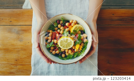 A vibrant Mediterranean bean salad with chickpeas, kidney beans, sun-dried tomatoes, and olives, served in a rustic ceramic bowl with olive oil and lemon. 123203414