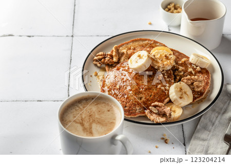 Healthy oatmeal pancakes with banana, nuts and honey on white tile background. Morning breakfast. Pancake day or Maslenitsa recipe, text space 123204214