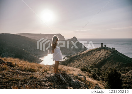 A woman stands on a hill overlooking a body of water. The sky is clear and the sun is shining brightly. The woman is enjoying the view and the peaceful atmosphere. 123205216