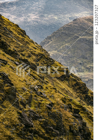 Rugged mountains rise sharply, displaying steep grassy slopes and rocky formations. The landscape is dramatic, shrouded in mist and offering a sense of isolation and beauty. 123207327