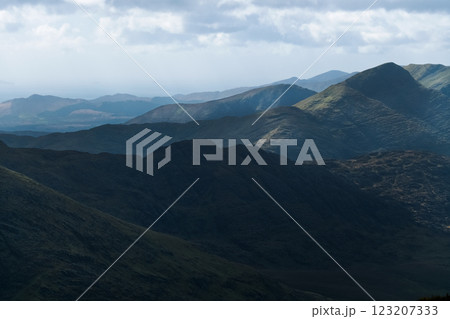 A panoramic view of a mountainous terrain. The color palette is muted, showcasing dark greens and grays. The overall mood is somber and atmospheric. 123207333