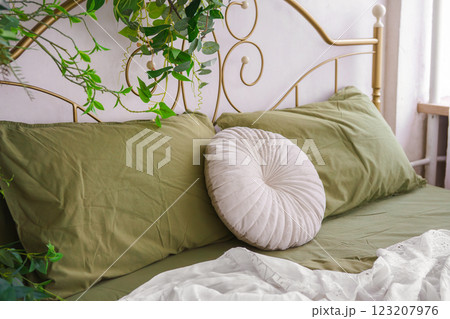Round white plush decorative pillow on bed with green bedding, home decor, bedroom interior 123207976