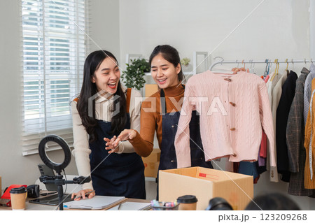Two young women collaborating in an online clothing business, showcasing a pink sweater and discussing sales strategies. 123209268