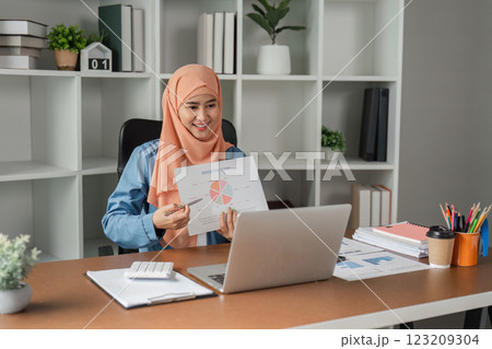Muslim woman in hijab presenting a report with a pie chart during a video call in a modern office. 123209304