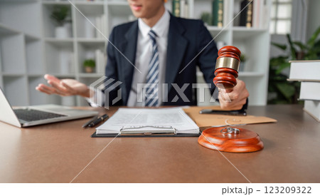 Lawyer explaining legal matters while holding gavel, engaged in discussion at modern office desk. Lawyer explaining legal matters while holding gavel, engaged in discussion at modern office desk. 123209322