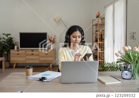 Focused woman working from home with laptop and smartphone, managing tasks and responsibilities. 123209332