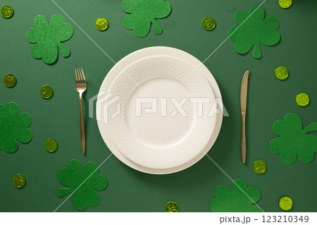 St Patrick's Day table setting with white plate and traditional decoration, shamrock, clover leaves and coins on dark green background. View from above. St Patrick's Day table setting with white plate and traditional decoration, shamrock, clover leaves and coins on dark green background. View from above. 123210349