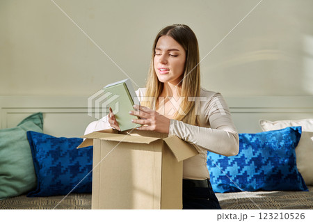 Young woman unpacking cardboard with online order, looking at new cosmetics perfumes 123210526