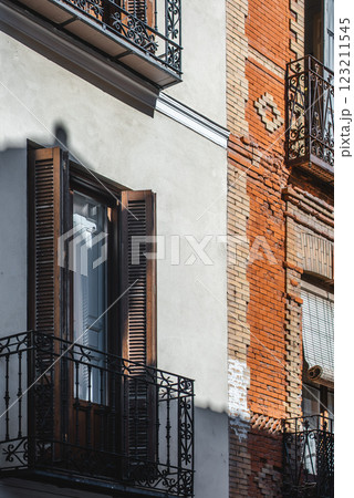 Two distinct sections of a building reveal ornate iron balconies and contrasting weathered brickwork bathed in warm sunlight during the day. Two distinct sections of a building reveal ornate iron balconies and contrasting weathered brickwork bathed in warm sunlight during the day. 123211545