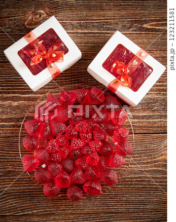 Sweets in the shape of strawberries and raspberries in festive packages. Wooden brown background. Sweets in the shape of strawberries and raspberries in festive packages. Wooden brown background. 123211581