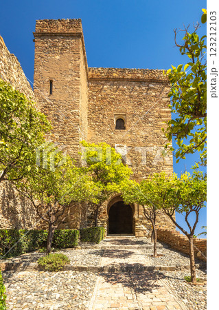 Alcazaba, palace and fortification in Malaga city at Andalusia, Spain, Europe. Ancient stone gateway, sunlight illuminating a pathway framed by lush green trees within a historic stone structure. 123212103
