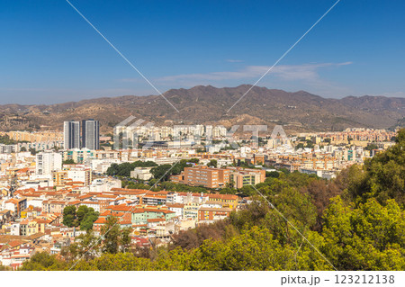 Malaga, seaside city in Andalusia, Spain, Europe. Panoramic view of a city nestled against mountains under a clear blue sky. Buildings, trees, and hills create a picturesque landscape. 123212138