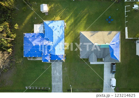 Aerial view of damaged in hurricane Ian houses roofs covered with blue protective tarp against rain water leaking until replacement of asphalt shingles Aerial view of damaged in hurricane Ian houses roofs covered with blue protective tarp against rain water leaking until replacement of asphalt shingles 123214625