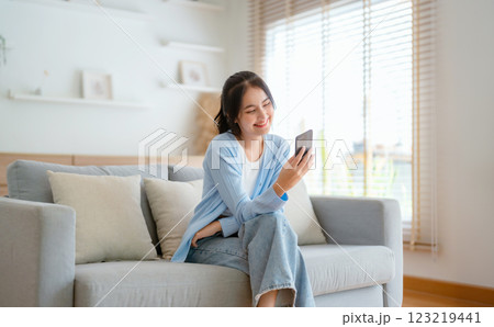 Smiling pretty young Asian woman sitting on cozy couch Smiling pretty young Asian woman sitting on cozy couch 123219441