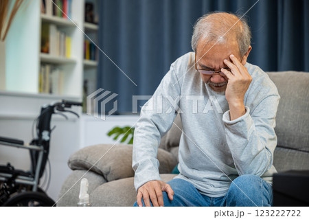 Asian mature old man sitting on sofa headache at home in living room, Depressed senior man unhappy hands rubbing eye suffering from a migraine. Health care 123222722