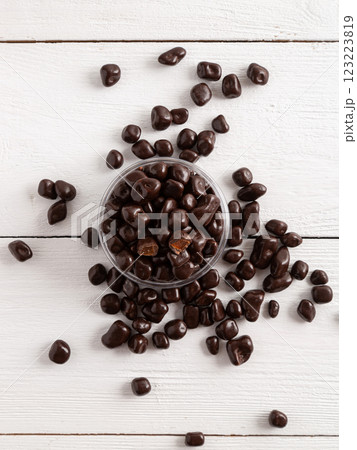 Dried fruits in brown chocolate. Candies on a white wooden background. 123223819